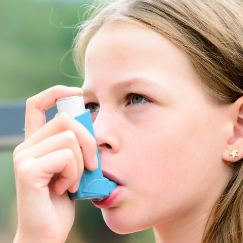 Girl having asthma using asthma inhaler for being healthy - shallow depth of field