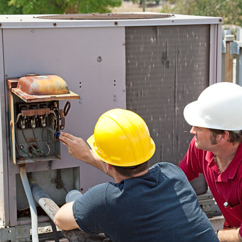 Two AC technicians on a roof repairing an industrial compressor unit.