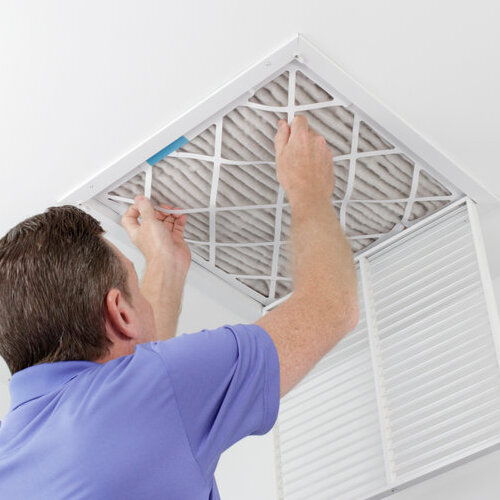 Caucasian male removing a square pleated dirty air filter with both hands from a ceiling air duct. Guy taking out an unclean air filter from a home ceiling air vent.