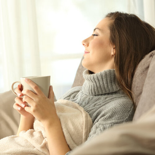 Portrait of a pensive woman relaxing sitting on a sofa in the living room in a house interior in winter